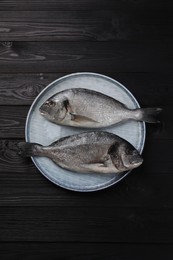 Photo of Fresh raw dorado fish on black wooden table, top view