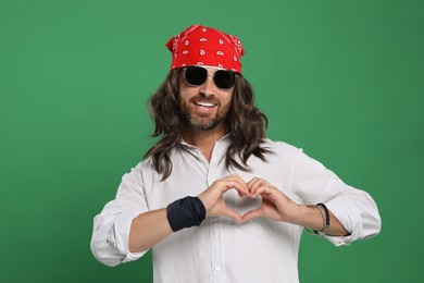 Photo of Hippie man in sunglasses making heart with hands on green background