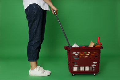 Photo of Woman with shopping basket full of different products on green background, closeup