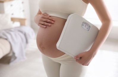 Photo of Young pregnant woman with scales at home, closeup