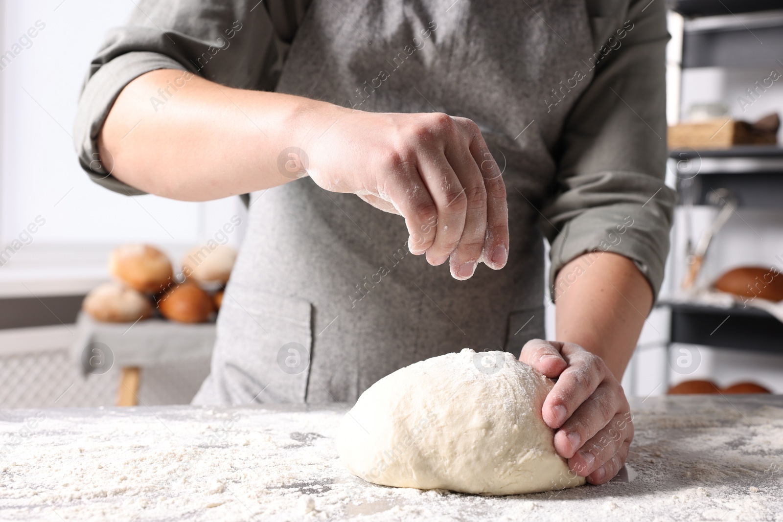 Photo of Man sprinkling flour over dough at table in kitchen, closeup