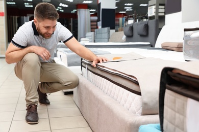 Young man choosing new orthopedic mattress in store