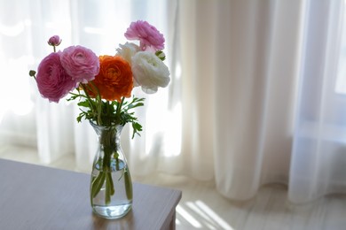 Bouquet of beautiful ranunculus flowers in vase on wooden table indoors. Space for text