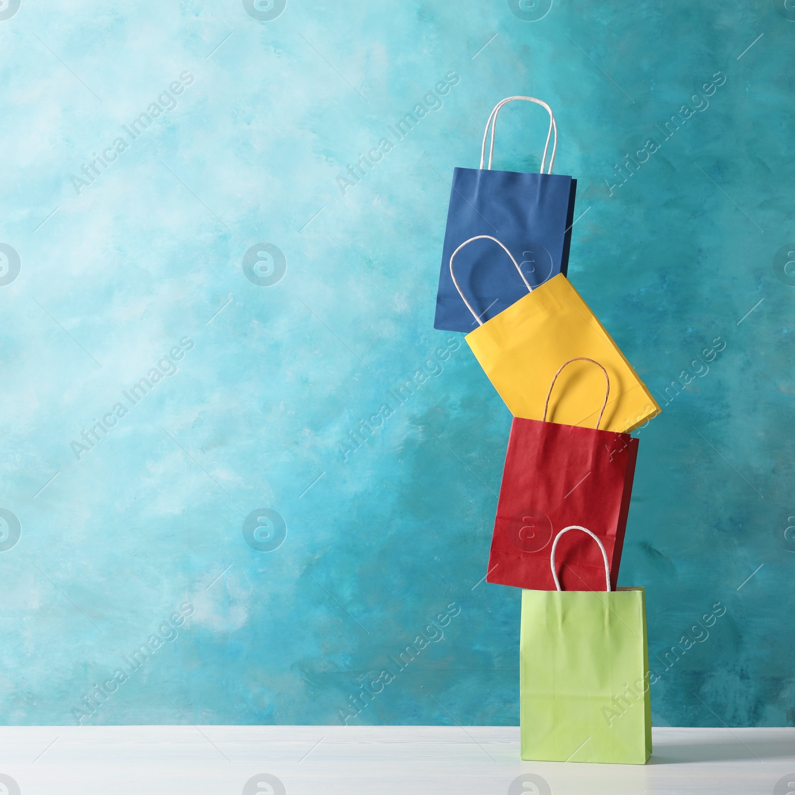 Photo of Colorful paper shopping bags on table against color background. Space for text