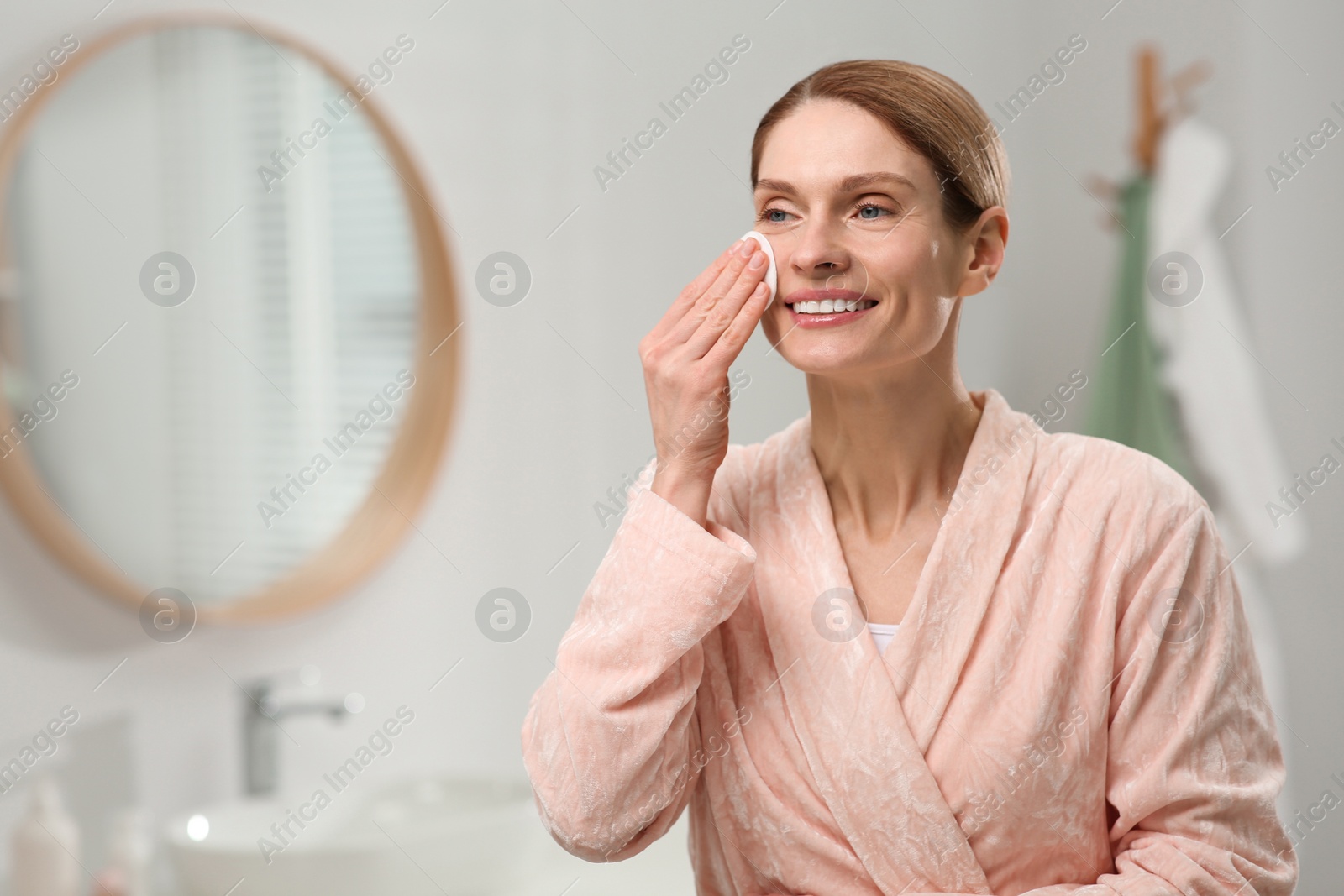 Photo of Beautiful woman removing makeup with cotton pad indoors, space for text