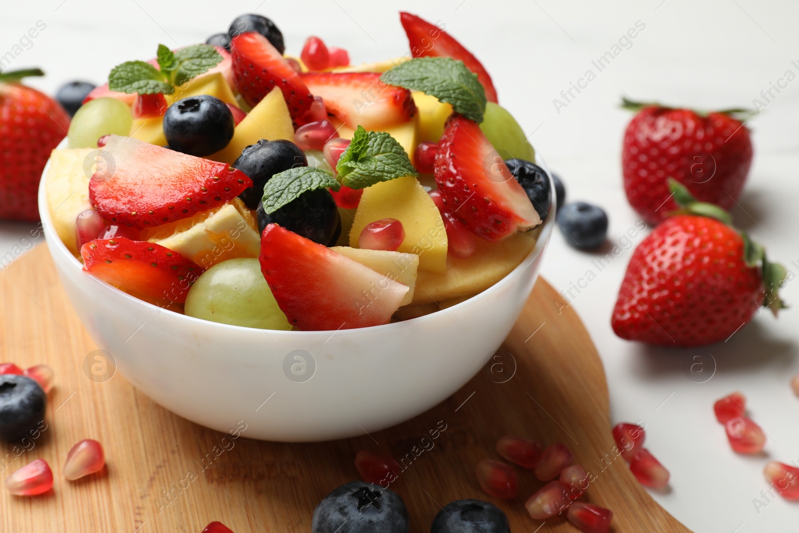 Photo of Tasty fruit salad in bowl and ingredients on white table, closeup