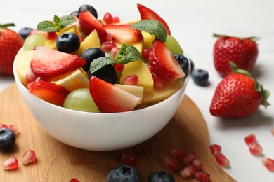 Photo of Tasty fruit salad in bowl and ingredients on white table, closeup