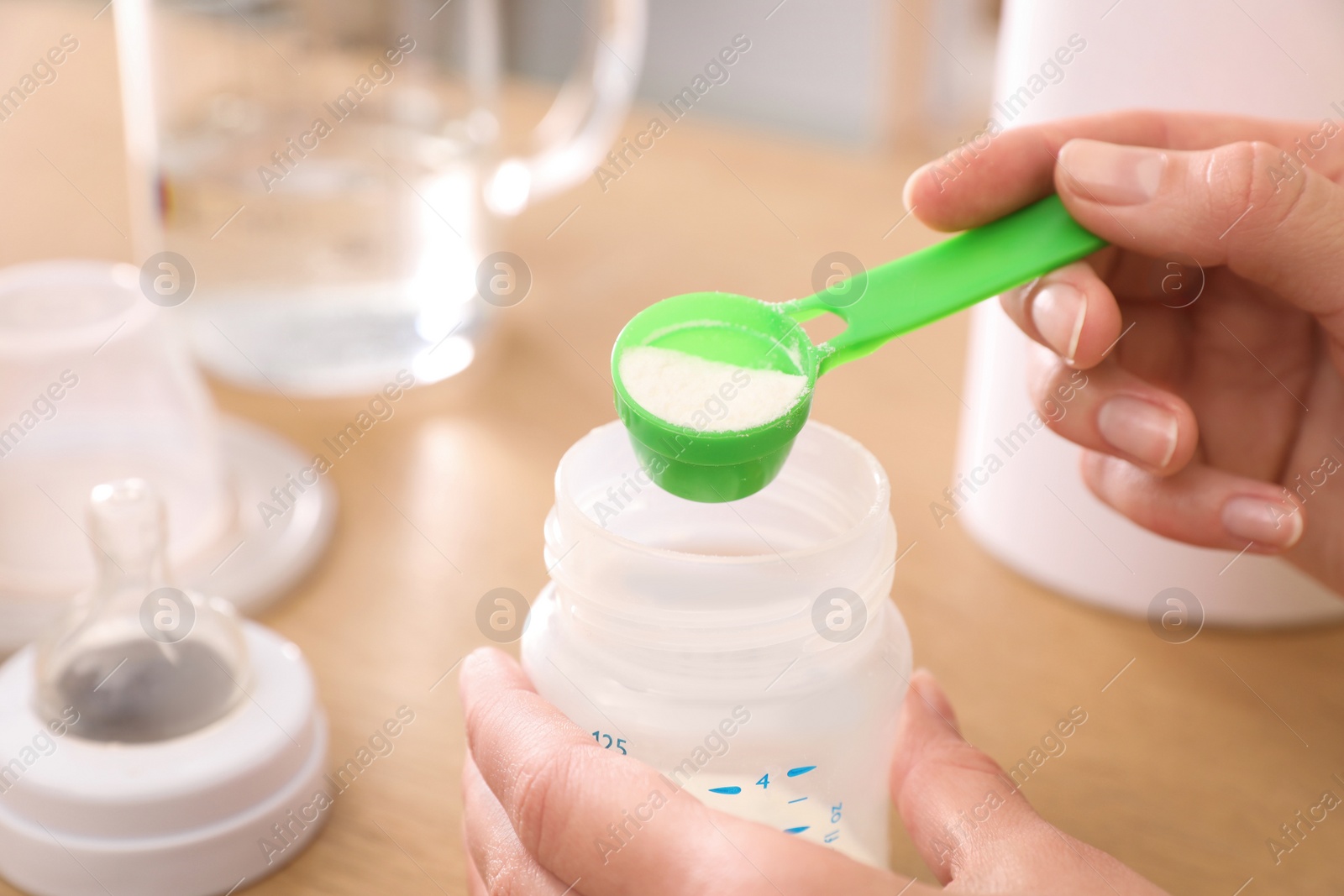 Photo of Woman preparing infant formula at table, closeup. Baby milk