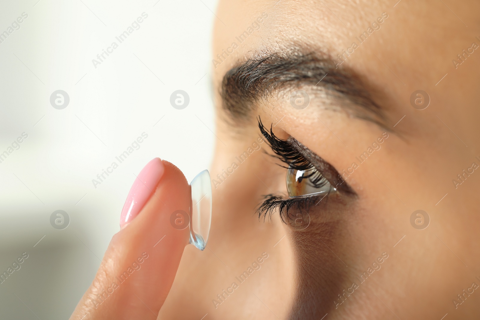 Photo of Young woman putting contact lens in her eye, closeup