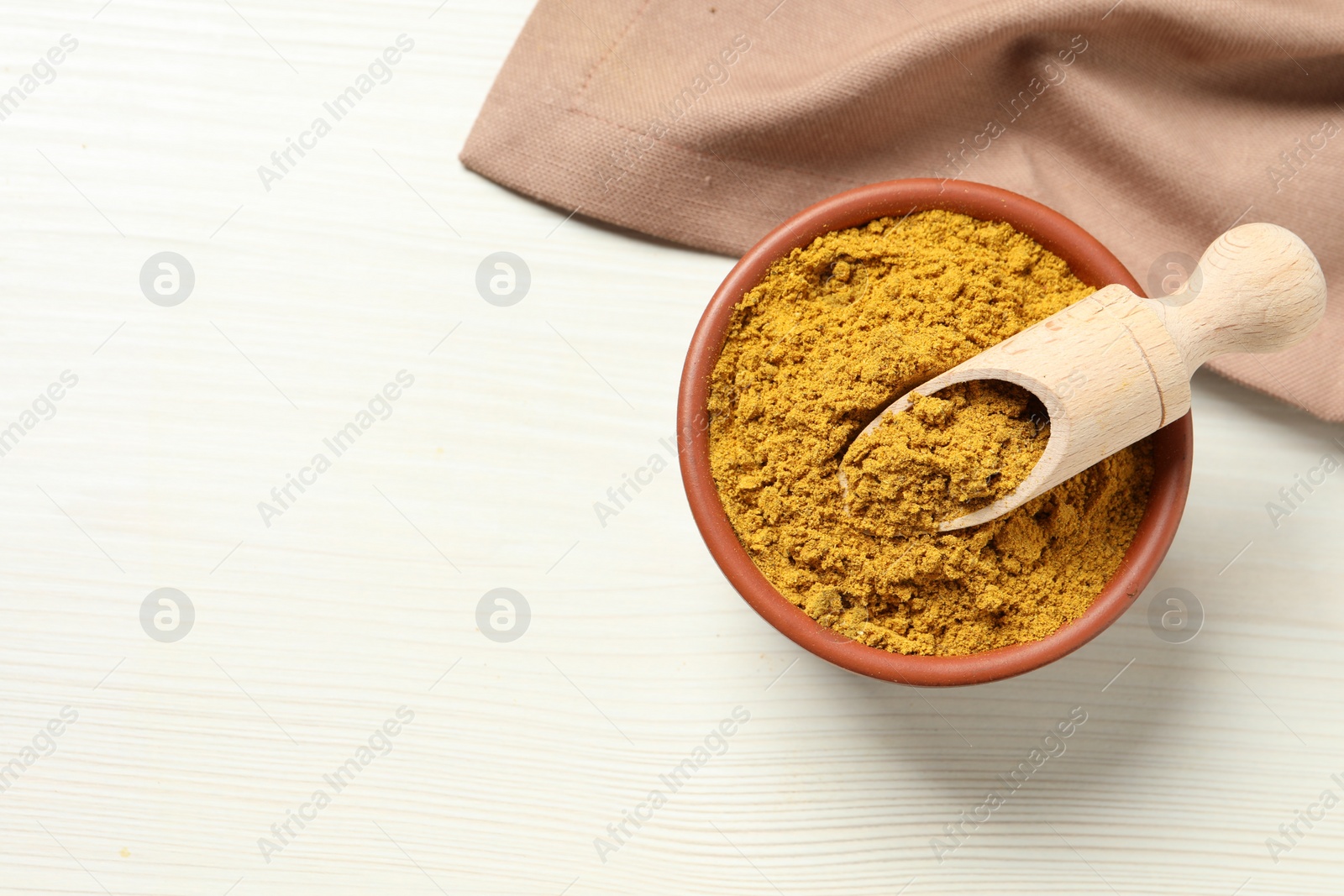 Photo of Curry powder in bowl and scoop on white wooden table, top view. Space for text