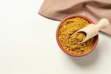 Photo of Curry powder in bowl and scoop on white wooden table, top view. Space for text
