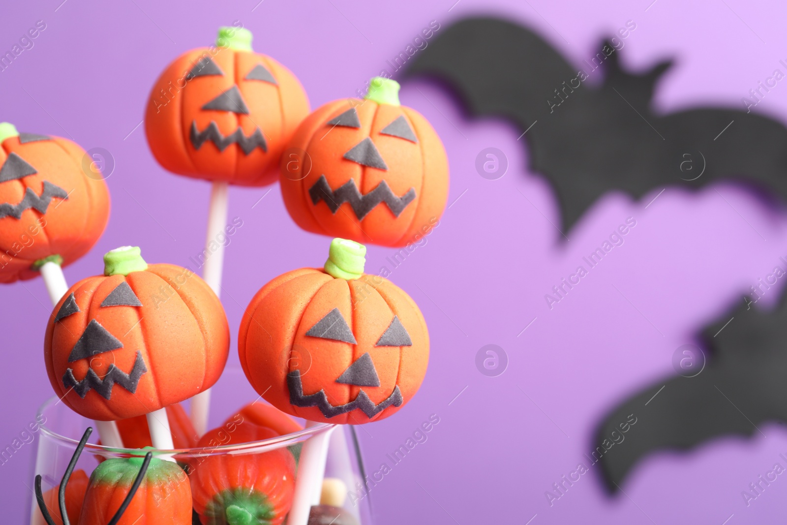 Photo of Delicious Halloween themed cake pops on violet background, closeup. Space for text