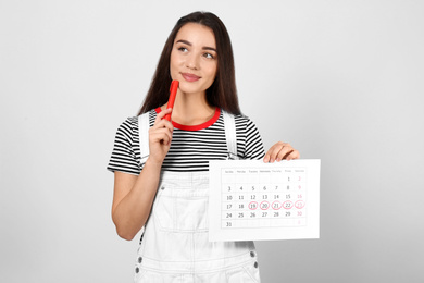 Photo of Young woman holding calendar with marked menstrual cycle days on light background