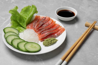 Photo of Sashimi set (salmon slices) with cucumber, greens, vasabi and funchosa served with soy sauce on light grey table