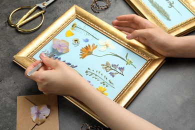 Photo of Woman making beautiful herbarium with pressed dried flower at black table, closeup