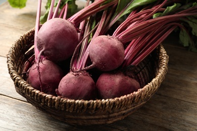 Photo of Raw ripe beets in wicker bowl on wooden table, closeup