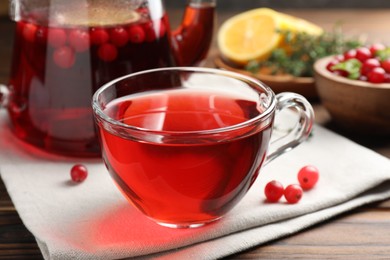 Photo of Tasty hot cranberry tea in glass cup and fresh berries on wooden table