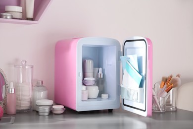 Photo of Mini fridge with cosmetic products on grey vanity table indoors