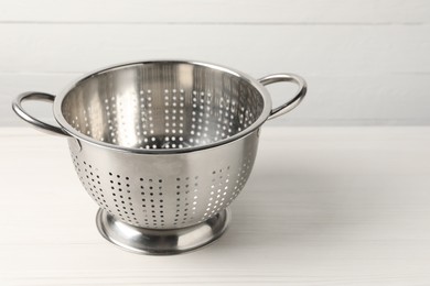 Photo of Metal colander on white wooden table. Space for text