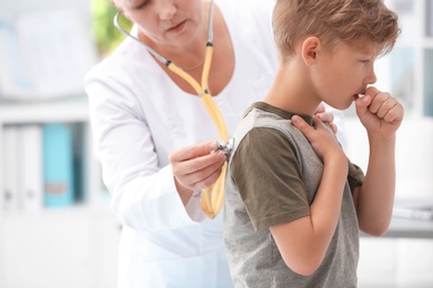 Photo of Doctor examining coughing little boy at clinic