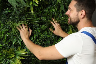 Photo of Smiling man installing green artificial plant panel on wall