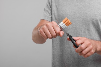 Photo of Stop smoking concept. Man cutting cigarettes on grey background, closeup. Space for text