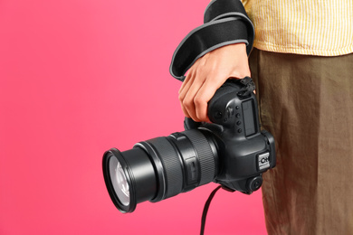 Photo of Professional photographer with modern camera on pink background in studio, closeup. Space for text