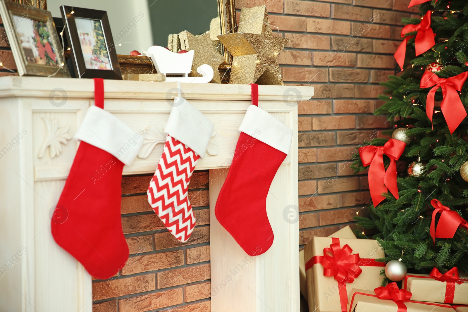 Photo of Decorative fireplace with stockings near beautiful Christmas tree and gifts indoors