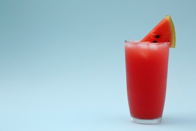 Photo of Delicious drink with ice cubes and piece of fresh watermelon on light blue background, space for text