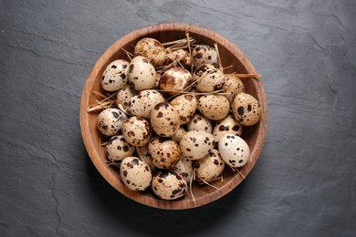 Photo of Bowl with quail eggs and straw on black table, top view