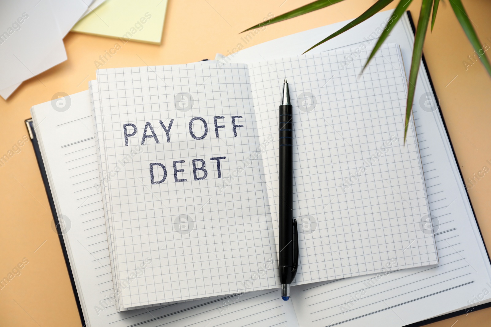 Image of Notebook with phrase Pay Off Debt and pen on beige background, flat lay