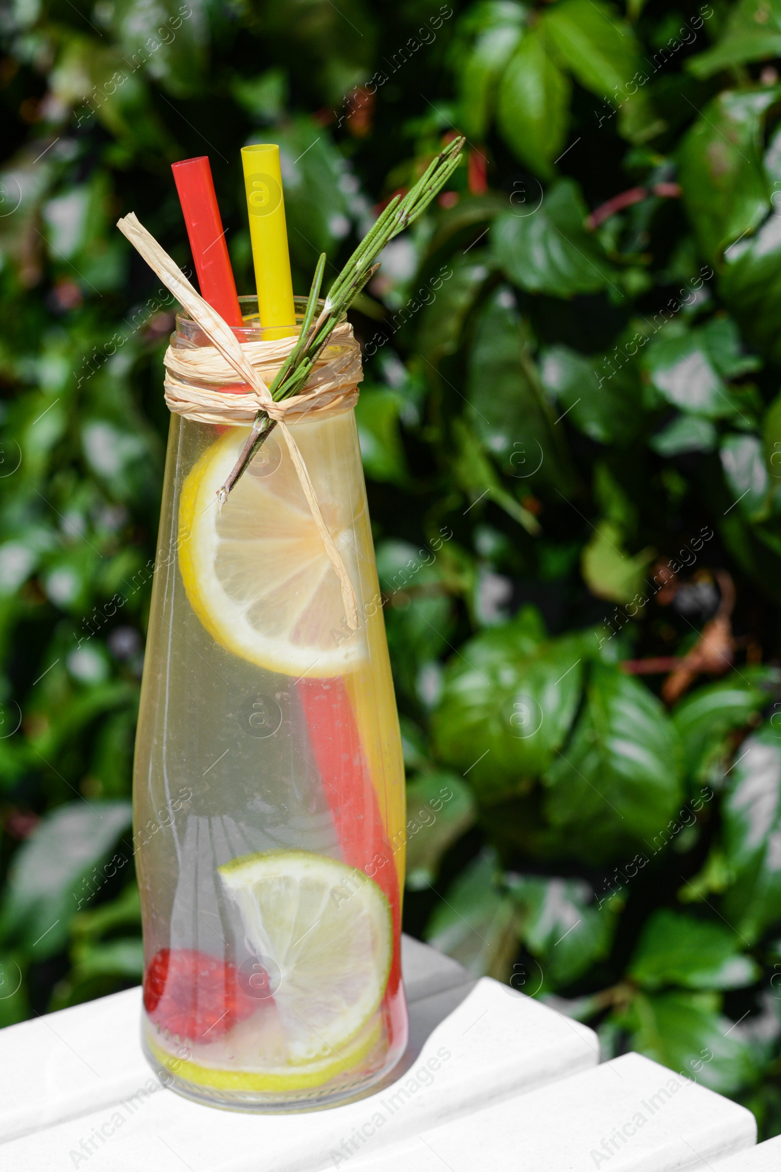 Photo of Refreshing tasty lemonade served in glass bottle on white wooden surface, closeup