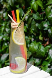 Photo of Refreshing tasty lemonade served in glass bottle on white wooden surface, closeup