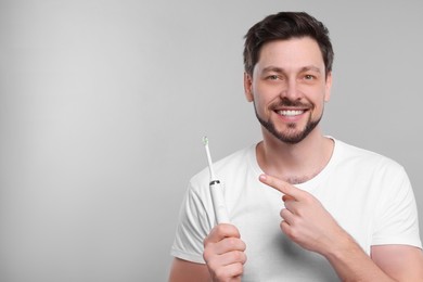 Happy man holding electric toothbrush on light grey background. Space for text