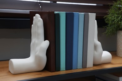 Photo of Beautiful hand shaped bookends with books on shelf indoors