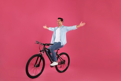 Handsome young man with modern bicycle on pink background