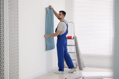 Photo of Man hanging light blue wallpaper in room