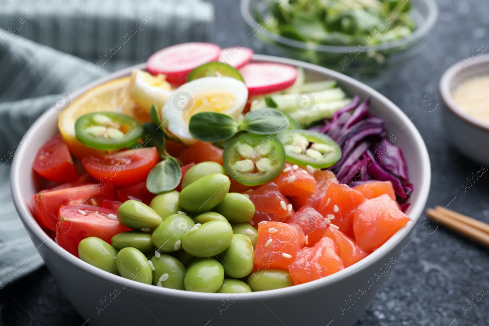 Photo of Poke bowl with salmon, edamame beans and vegetables on black table, closeup