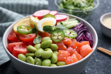 Photo of Poke bowl with salmon, edamame beans and vegetables on black table, closeup