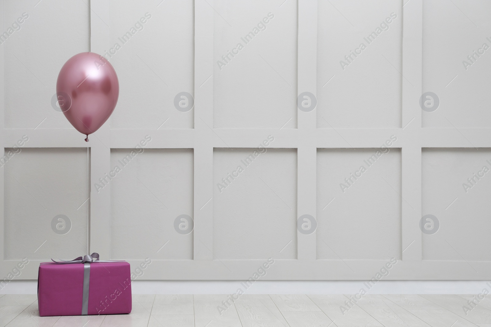 Photo of Gift box and balloon near white wall. Space for text