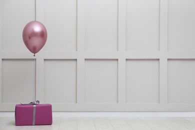 Photo of Gift box and balloon near white wall. Space for text