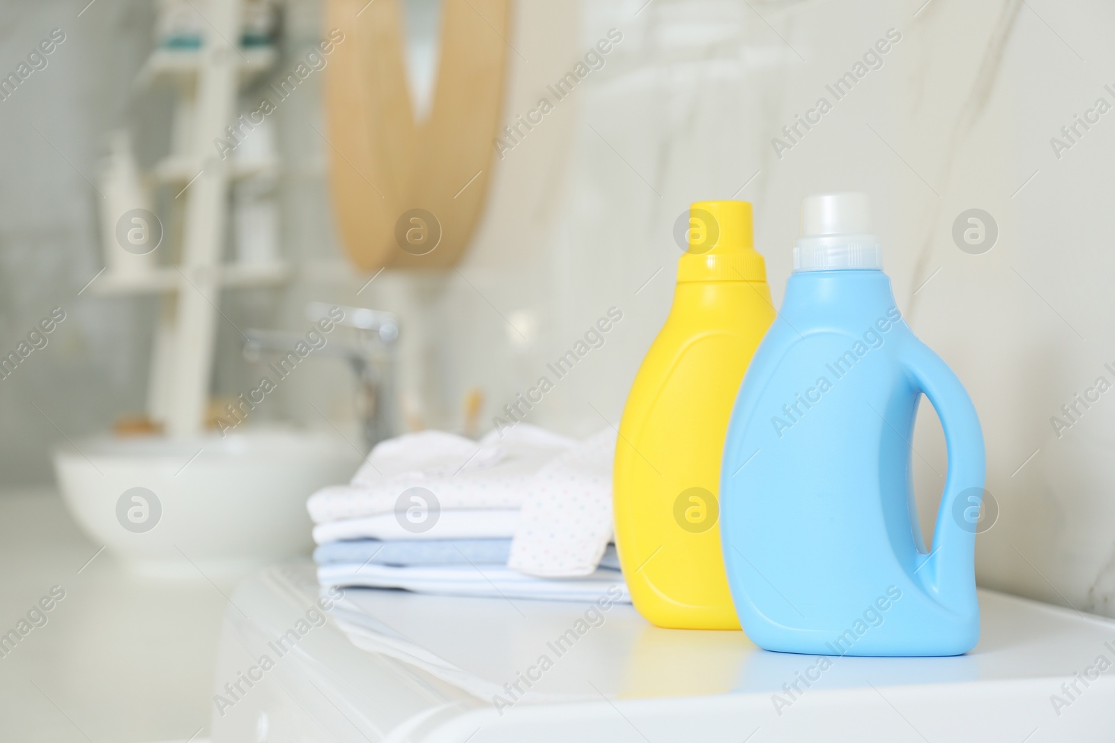 Photo of Bottles of detergent and children's clothes on countertop in bathroom. Space for text