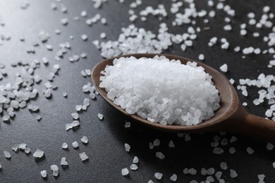 Photo of Natural salt and wooden spoon on black table, closeup