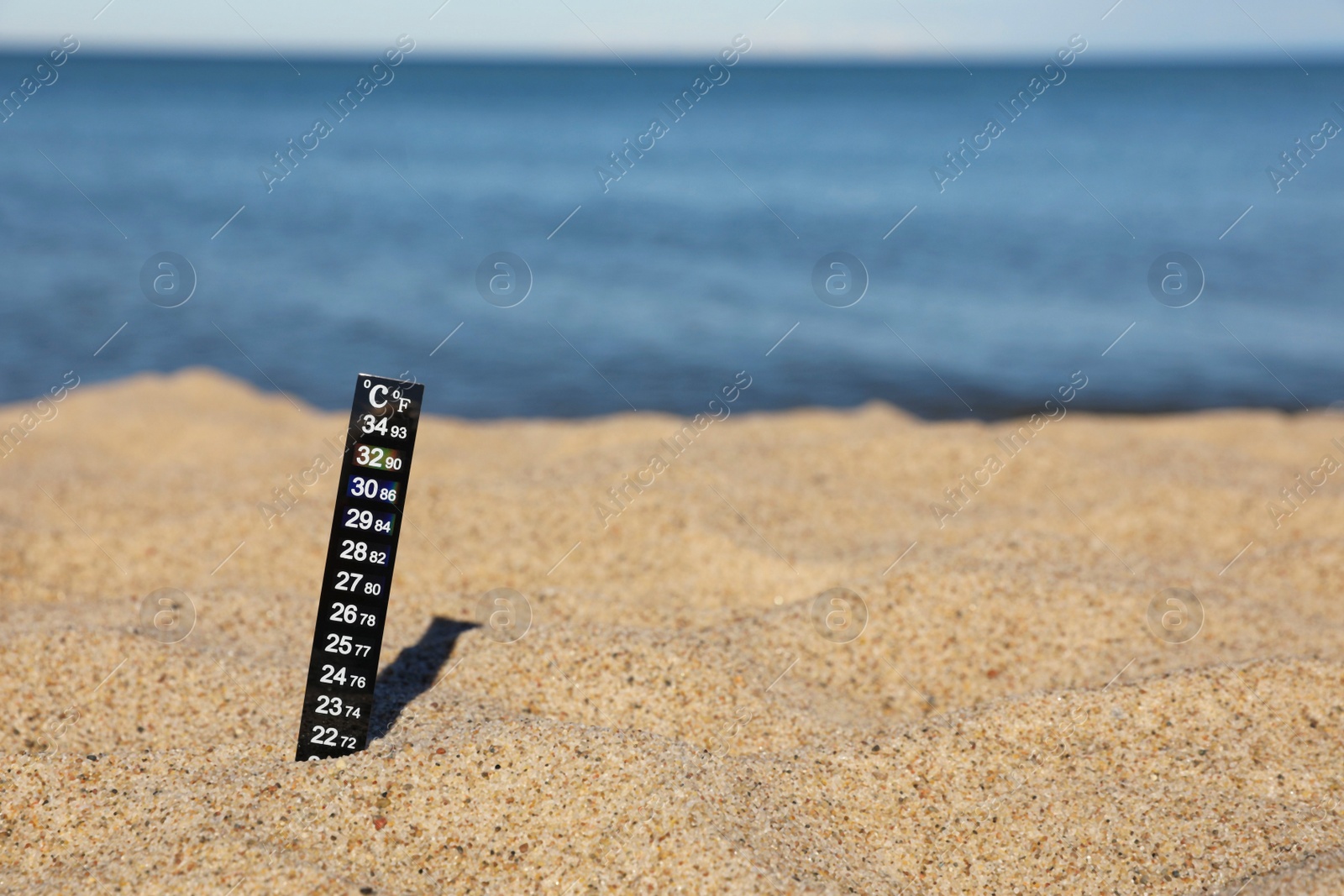 Photo of Weather thermometer in sand near sea, space for text