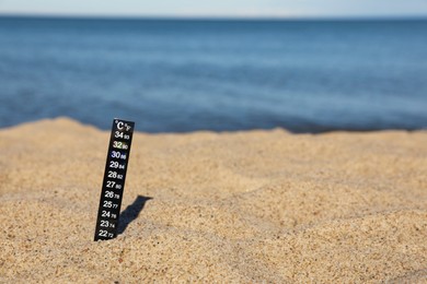 Weather thermometer in sand near sea, space for text