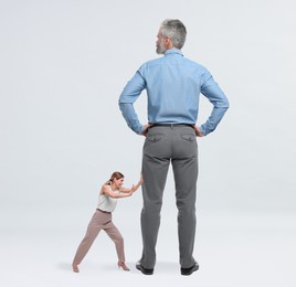 Image of Small woman pushing giant man on light background