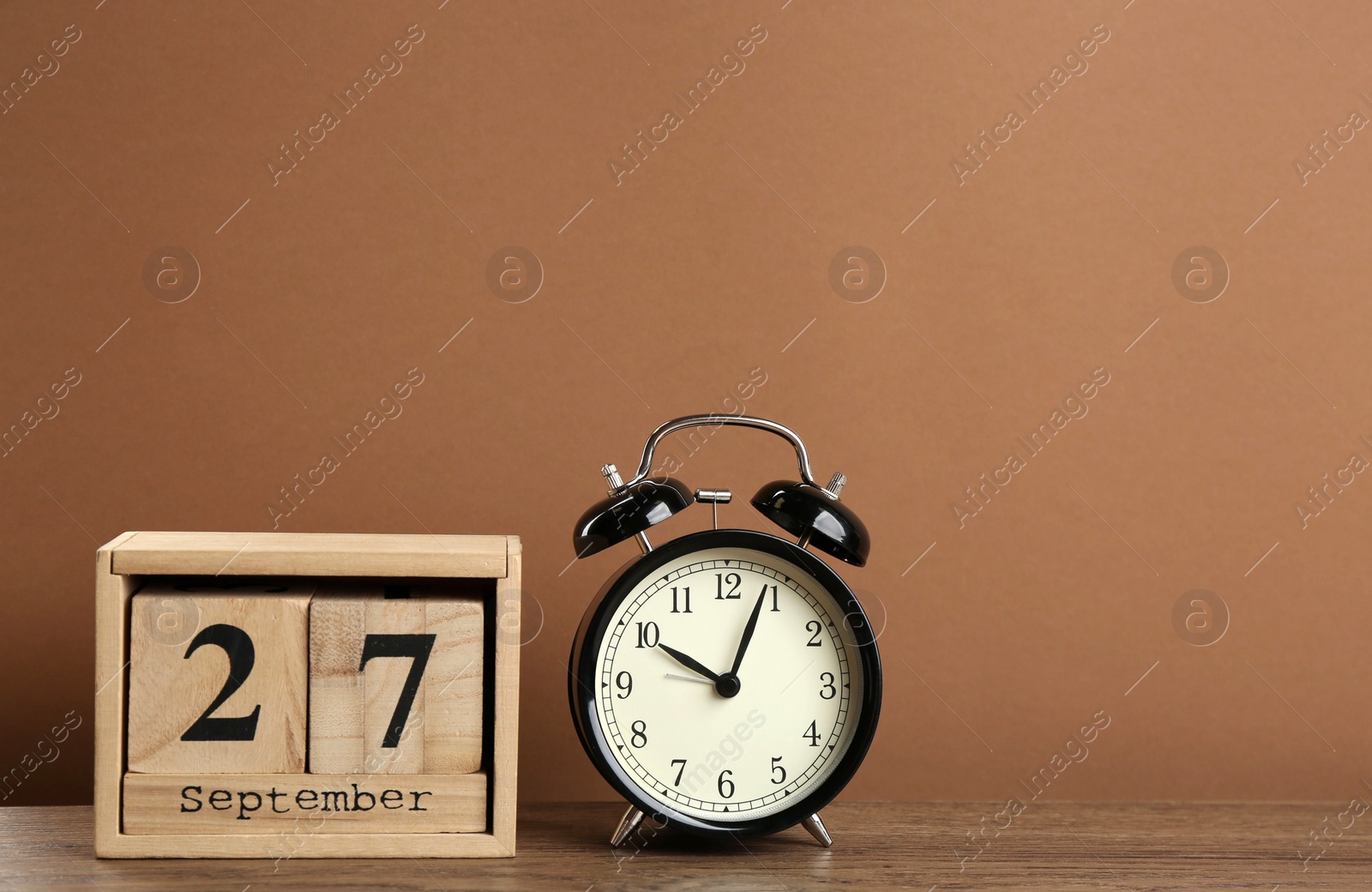 Photo of Wooden block calendar and alarm clock on table against brown background