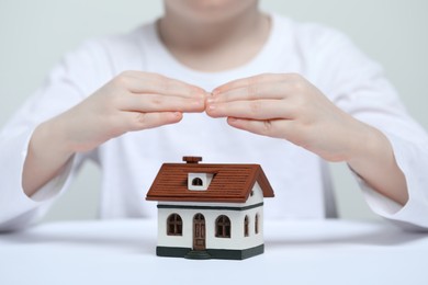 Photo of Home security concept. Little child covering house model at white table, closeup