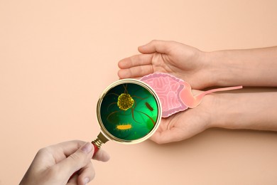 Microorganisms research. Women with magnifying glass and paper intestine cutout on beige background, closeup 