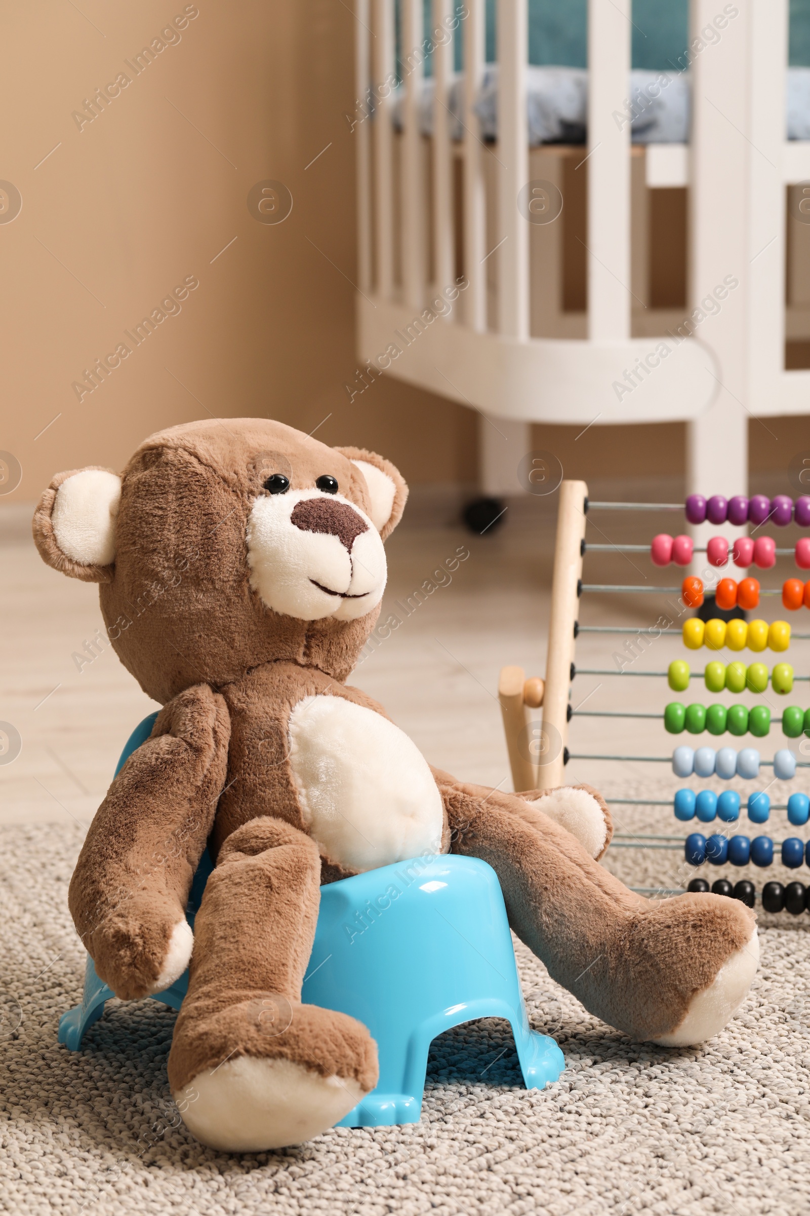 Photo of Teddy bear on light blue baby potty and toys in room. Toilet training
